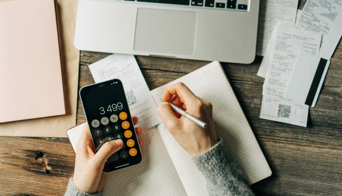 Top view of a work desk on which a woman keeps a budget using a calculator.